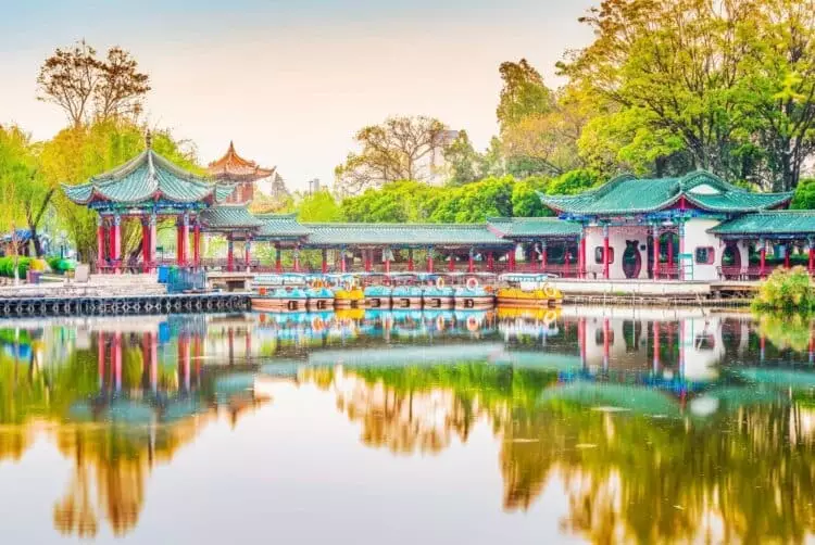 Pavillons traditionnels chinois au bord d’un plan d’eau entouré de végétation dans un jardin paysager en Chine