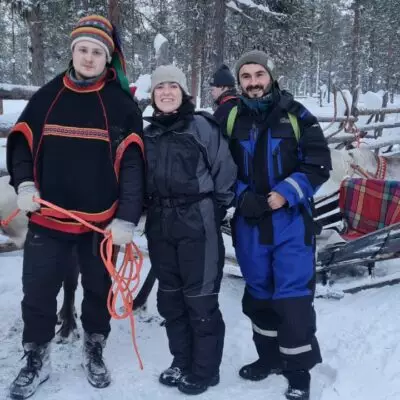 Voyageurs en tenue grand froid aux côtés de rennes et de traîneaux dans un paysage enneigé de Laponie.