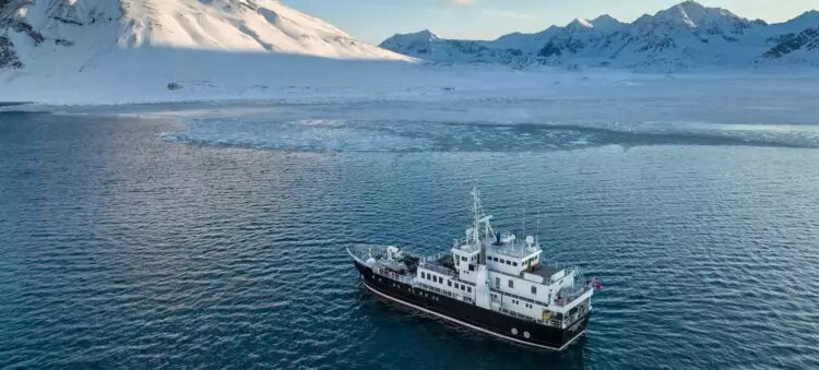 Navire d’expédition naviguant le long des côtes montagneuses enneigées du Groenland.