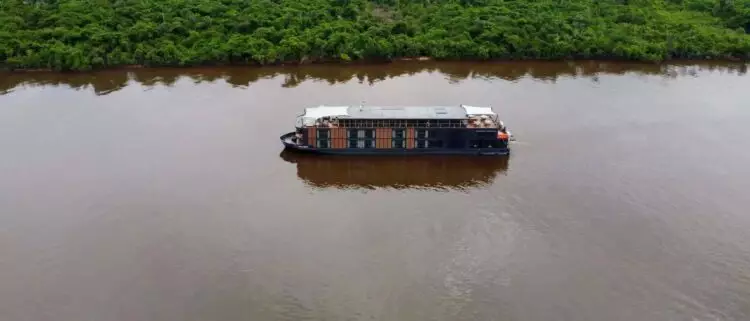 Bateau lodge naviguant sur un large fleuve en pleine Amazonie peruvienne entoure de foret tropicale dense.