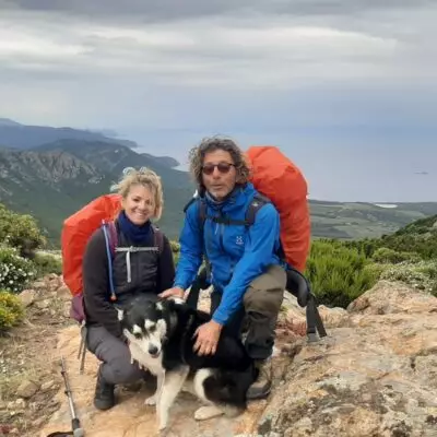 Couple de randonneurs avec leur chien profitant d’un panorama sur les montagnes et le littoral de la Corse.