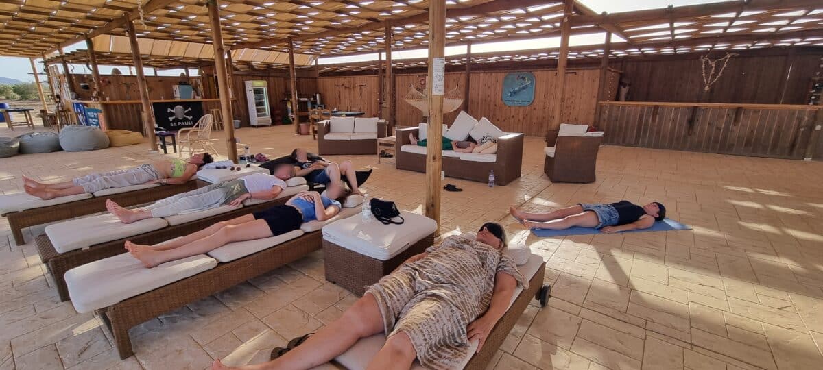 Participants en pleine relaxation sous une pergola face à la mer.