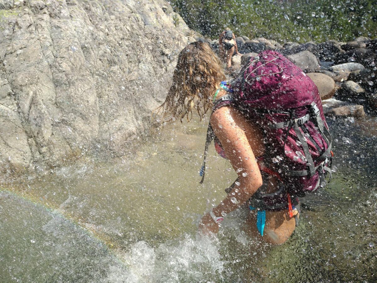 Randonneuse traversant un ruisseau éclaboussée par l'eau.