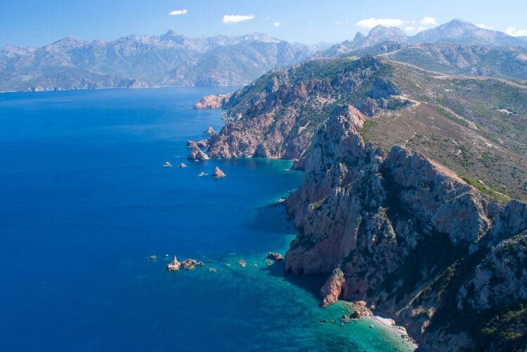 Vue panoramique des falaises rocheuses de la côte corse plongeant dans la mer.