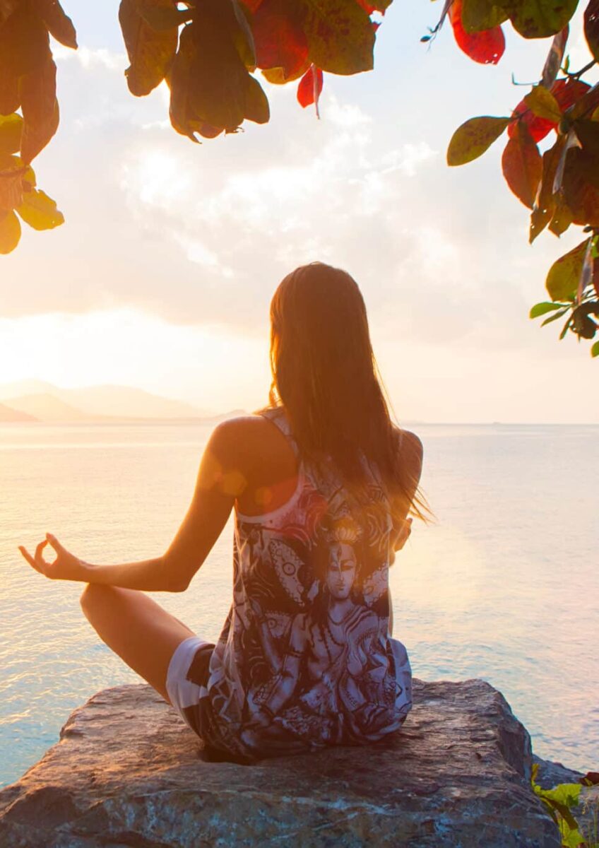 Femme méditant au bord de la mer pendant le coucher de soleil.