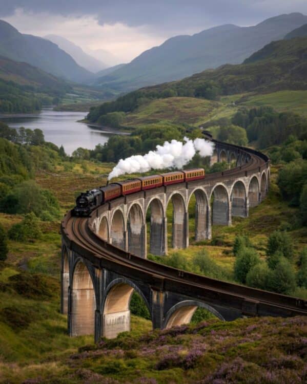 Train à vapeur traversant le viaduc de Glenfinnan au milieu des paysages des Highlands avec lac et montagnes en arrière-plan