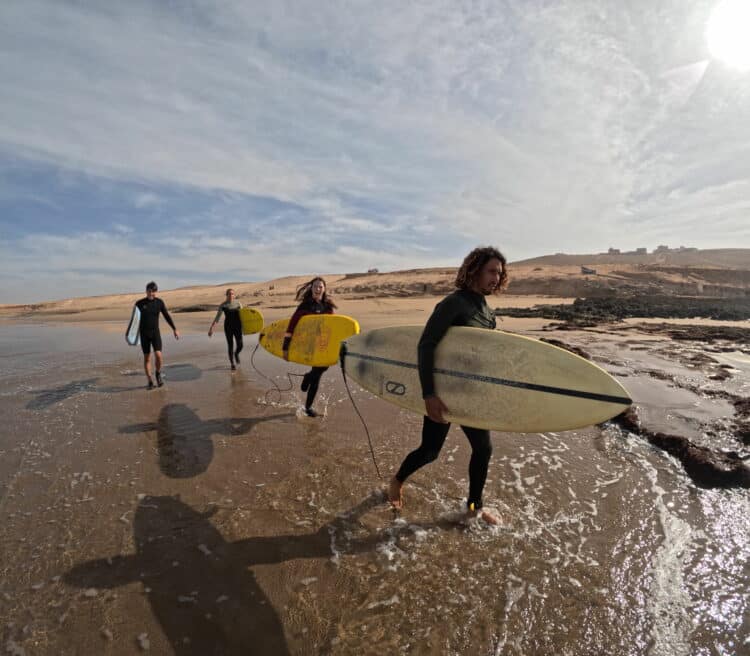 Groupe de surfeurs marchant sur la plage au Maroc - Surf Trip Itinérant.