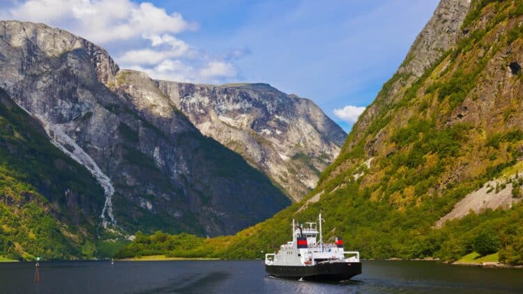 Ferry naviguant sur le Sognefjord entre de hautes montagnes verdoyantes en Norvège.