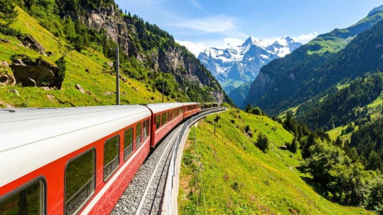 Train panoramique rouge traversant les Alpes suisses au cœur d’une vallée verdoyante