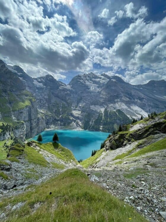 Lac de montagne suisse entouré de falaises et de sentiers de randonnée sous un ciel nuageux