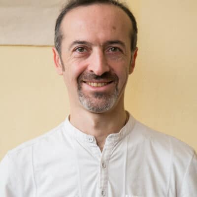 Portrait d’un homme en chemise blanche, sourire bienveillant.