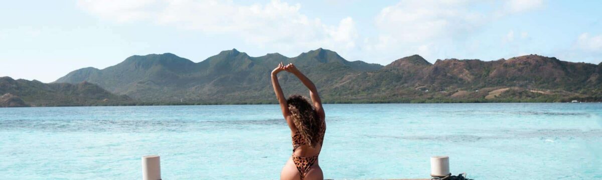 Femme assise sur un ponton en bois face à une mer turquoise et des montagnes en Colombie.