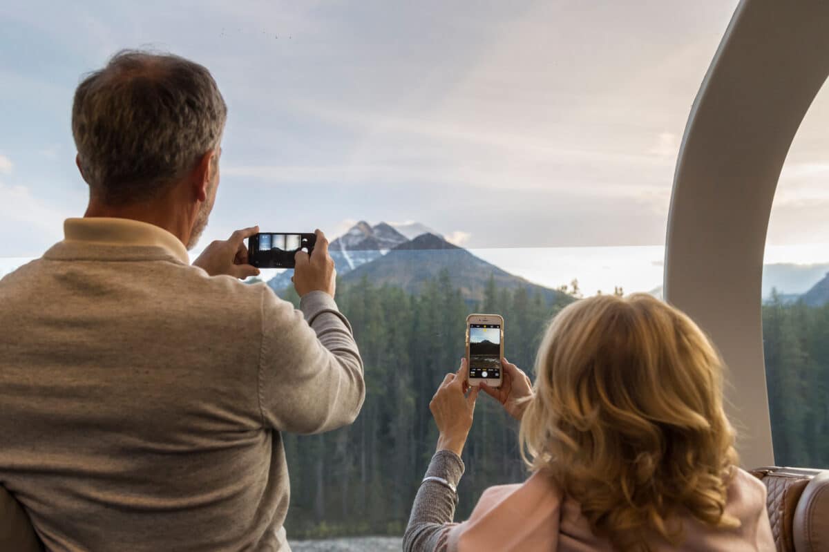 Un couple photographiant les sommets enneigés des Rocheuses canadiennes à travers les grandes baies vitrées du train.