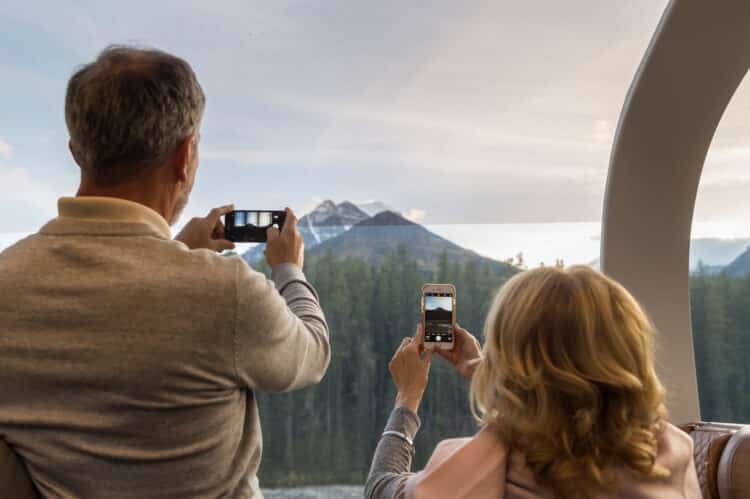 Un couple photographiant les sommets enneigés des Rocheuses canadiennes à travers les grandes baies vitrées du train.