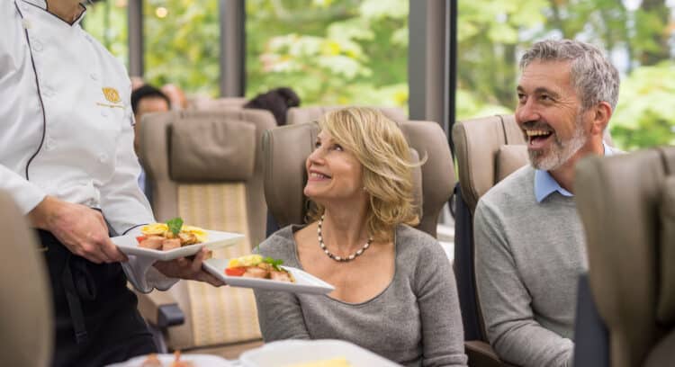 Service d’un repas raffiné à bord du train Rocky Mountaineer avec un couple profitant d’une cuisine gastronomique.