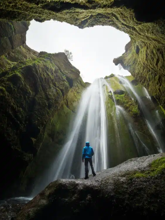 Un randonneur explore une cascade cachée en Islande dans une grotte naturelle.
