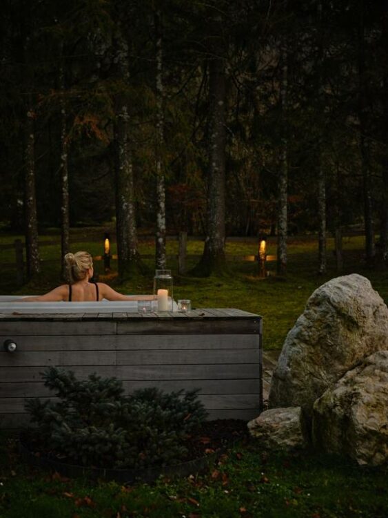 Femme profitant d’un bain nordique en extérieur à la tombée de la nuit, entourée de forêt
