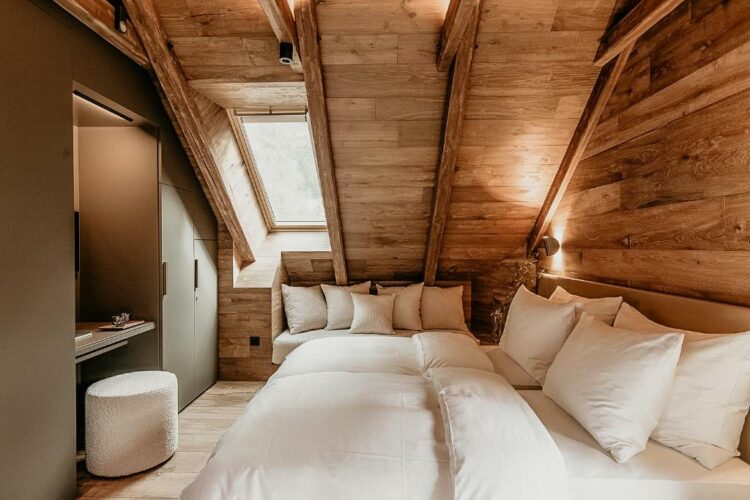 Chambre à l’ambiance chaleureuse sous les combles avec poutres apparentes et literie blanche