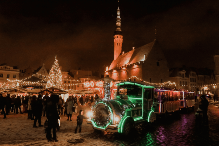 Marché de Noël illuminé sur une place médiévale d’Europe du Nord, avec sapin géant et animations