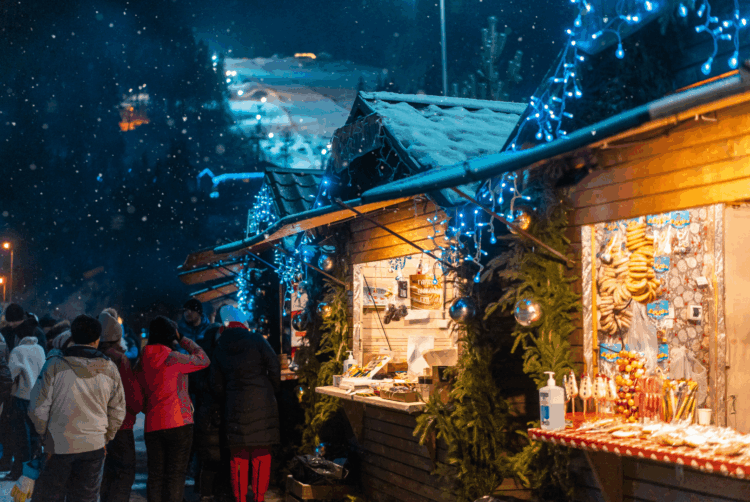Marché de Noël sous la neige dans le Grand Nord, avec chalets illuminés et ambiance hivernale.