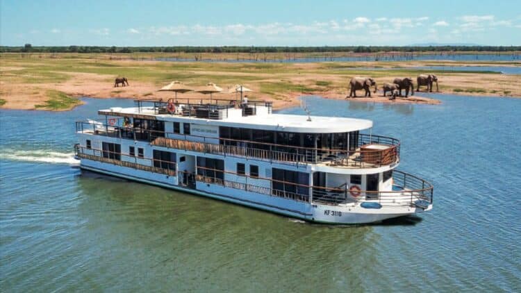 Bateau African Dream naviguant sur un fleuve africain lors d’une croisiere safari avec elephants visibles sur la berge.