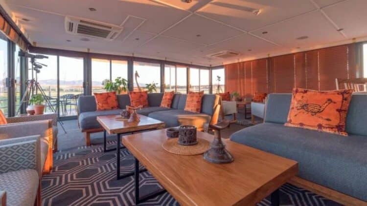 Salon panoramique du bateau African Dream avec canapes et grandes baies vitrees sur le fleuve africain.