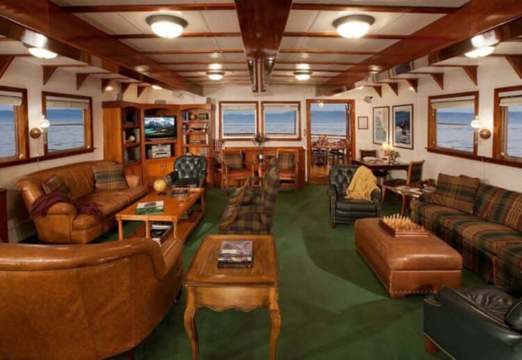 Salon panoramique avec fauteuils en cuir et grandes fenêtres à bord d’un bateau en Alaska.
