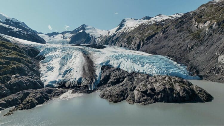 Glacier descendant entre des montagnes rocheuses enneigées en Alaska sous un ciel dégagé.