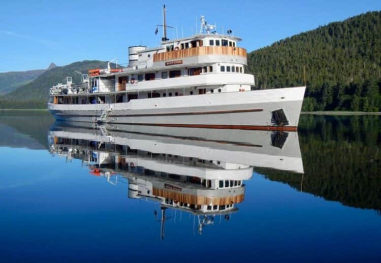 Navire d’expédition Mist Cove naviguant sur une mer calme entourée de forêts en Alaska.