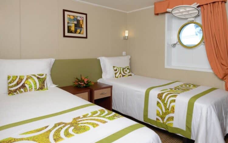 Cabine à deux lits du bateau Aranui avec décoration polynésienne et hublot donnant sur l’océan.