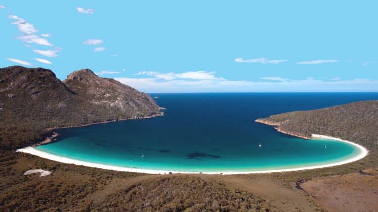 Vue panoramique d’une baie en Tasmanie avec plage de sable blanc et eau turquoise entourée de collines sauvages en Australie.