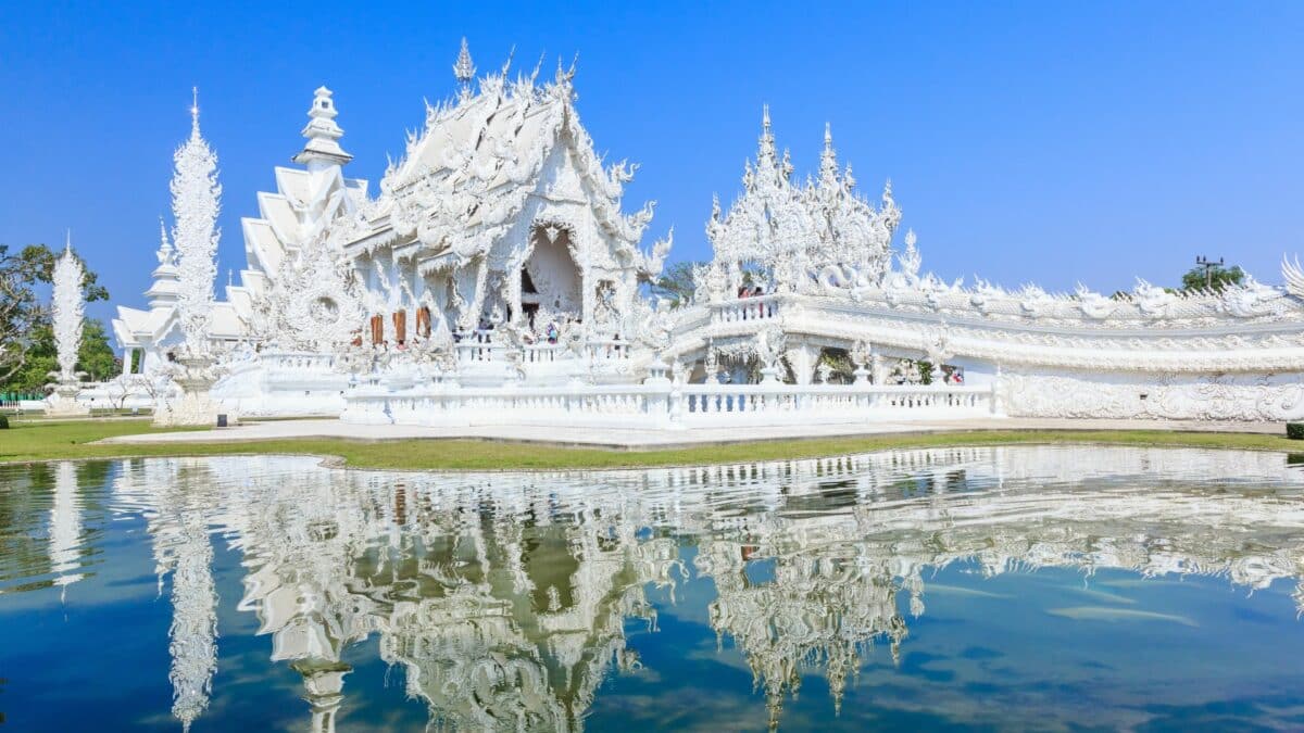 Wat Rong Khun, temple blanc de Chiang Rai, avec façade sculptée et reflet dans un bassin.
