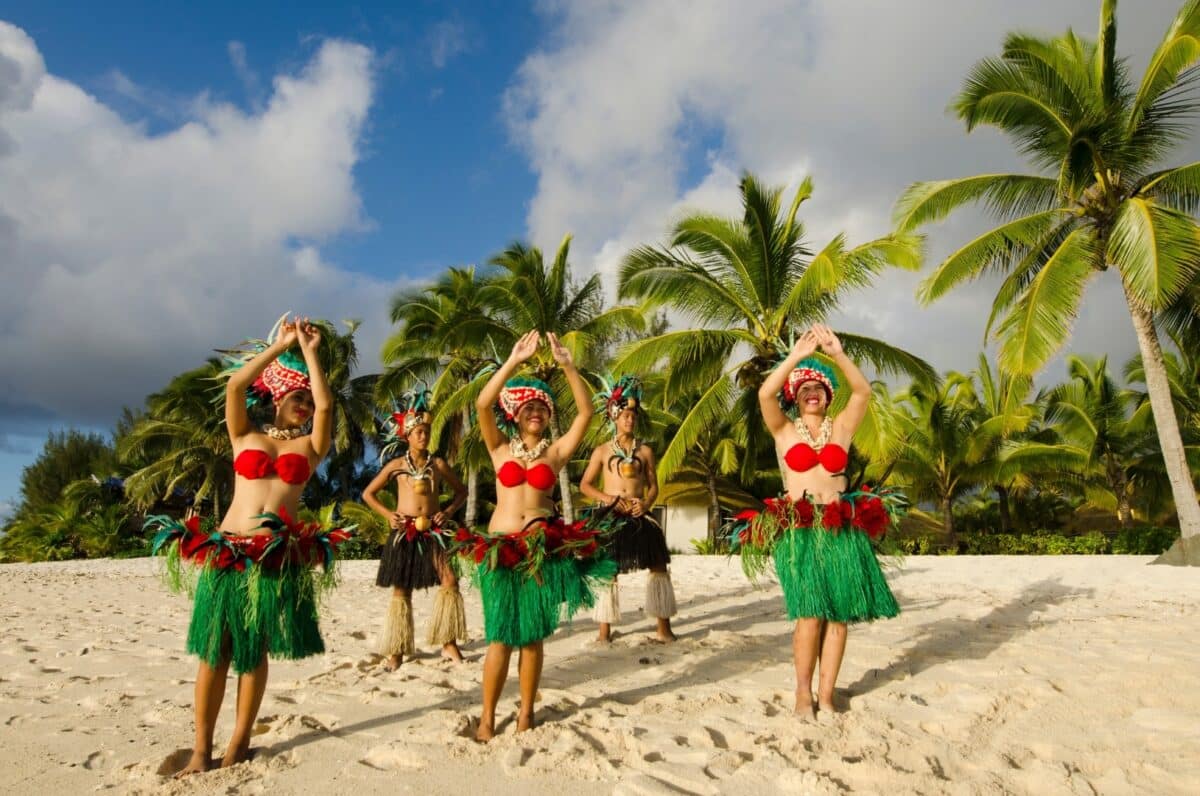 Danseuses polynésiennes en tenue traditionnelle sur une plage bordée de palmiers