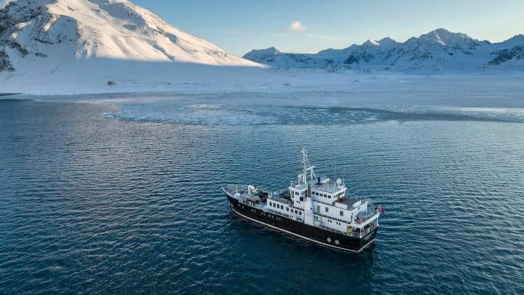 Navire d’expédition naviguant le long des côtes montagneuses enneigées du Groenland.