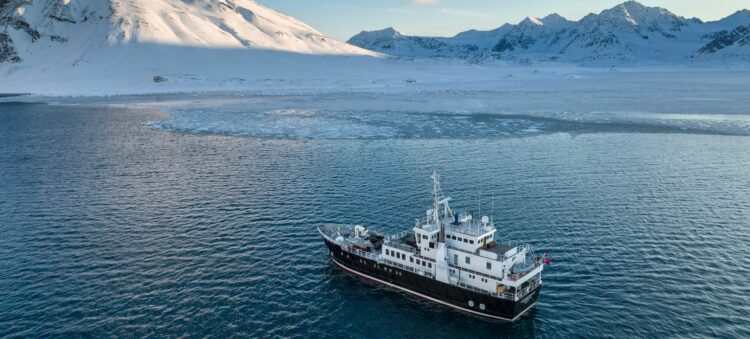 Navire d’expédition naviguant le long des côtes montagneuses enneigées du Groenland.