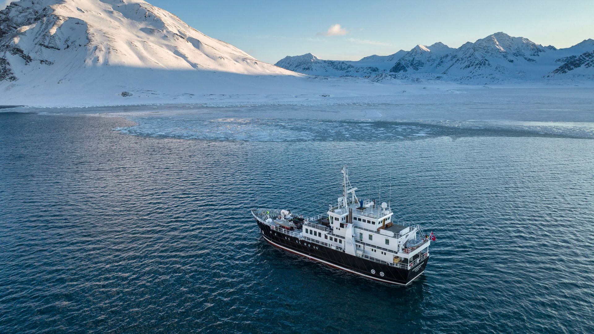 Navire d’expédition naviguant le long des côtes montagneuses enneigées du Groenland.