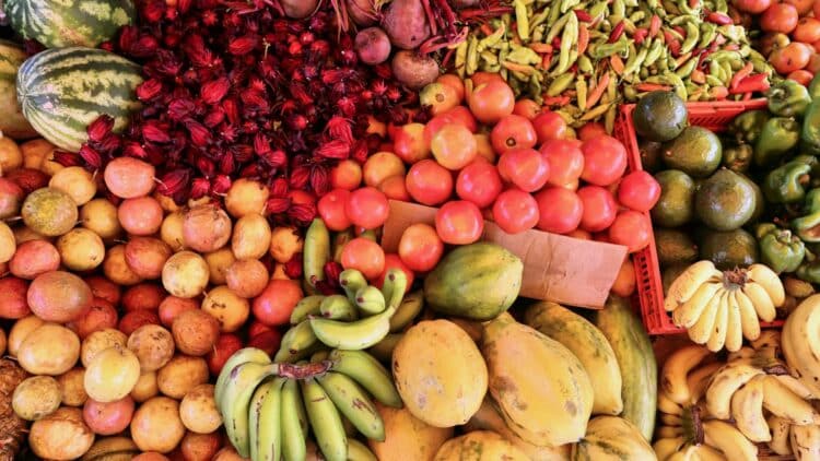 Étals colorés de fruits tropicaux de saison sur un marché local en Guadeloupe, avec bananes, papayes, tomates et piments.