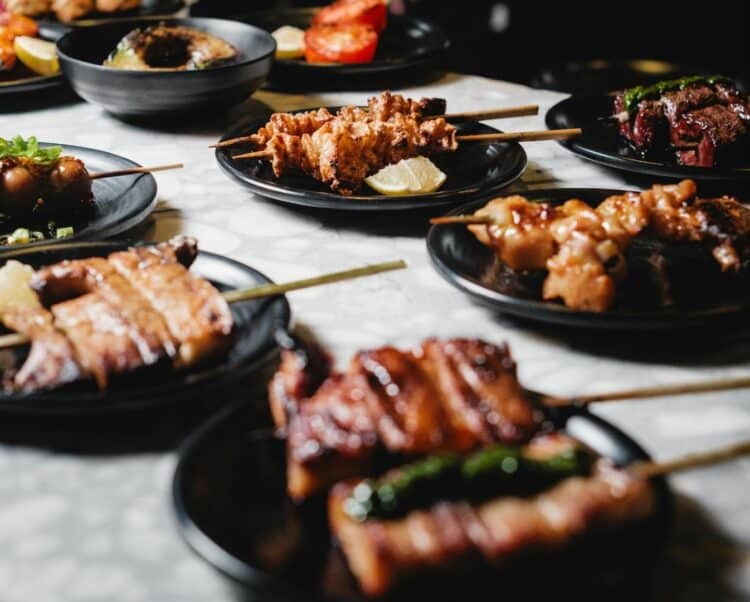 Assortiment de yakitori et spécialités grillées japonaises servis sur des assiettes noires.