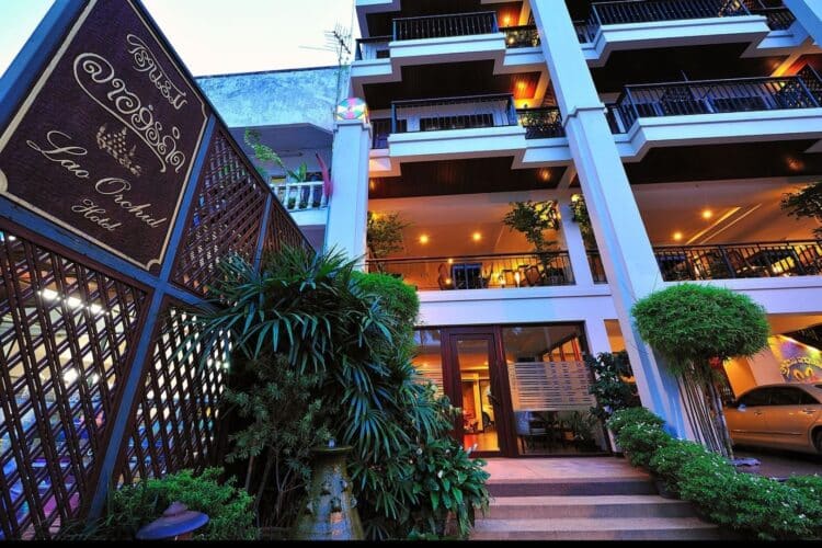 Façade du Lao Orchid Hotel à Vientiane avec balcons, végétation et entrée éclairée en soirée.