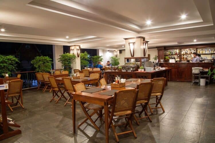 Salle de restaurant du Lao Orchid Hotel avec tables en bois, chaises et espace buffet.