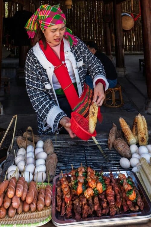 Stand de street food au Laos proposant brochettes grillées, saucisses et maïs.