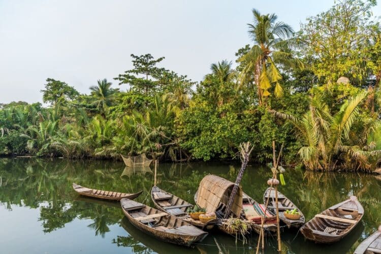 Barques traditionnelles amarrées sur une rivière entourée de végétation tropicale au Laos.