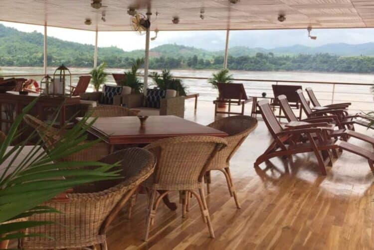 Terrasse panoramique d’un bateau de croisière sur le Mékong avec transats et vue sur les collines.