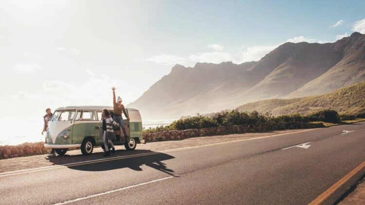 Voyageurs en van vintage sur une route côtière bordée de montagnes en Nouvelle-Zélande lors d’un road trip.