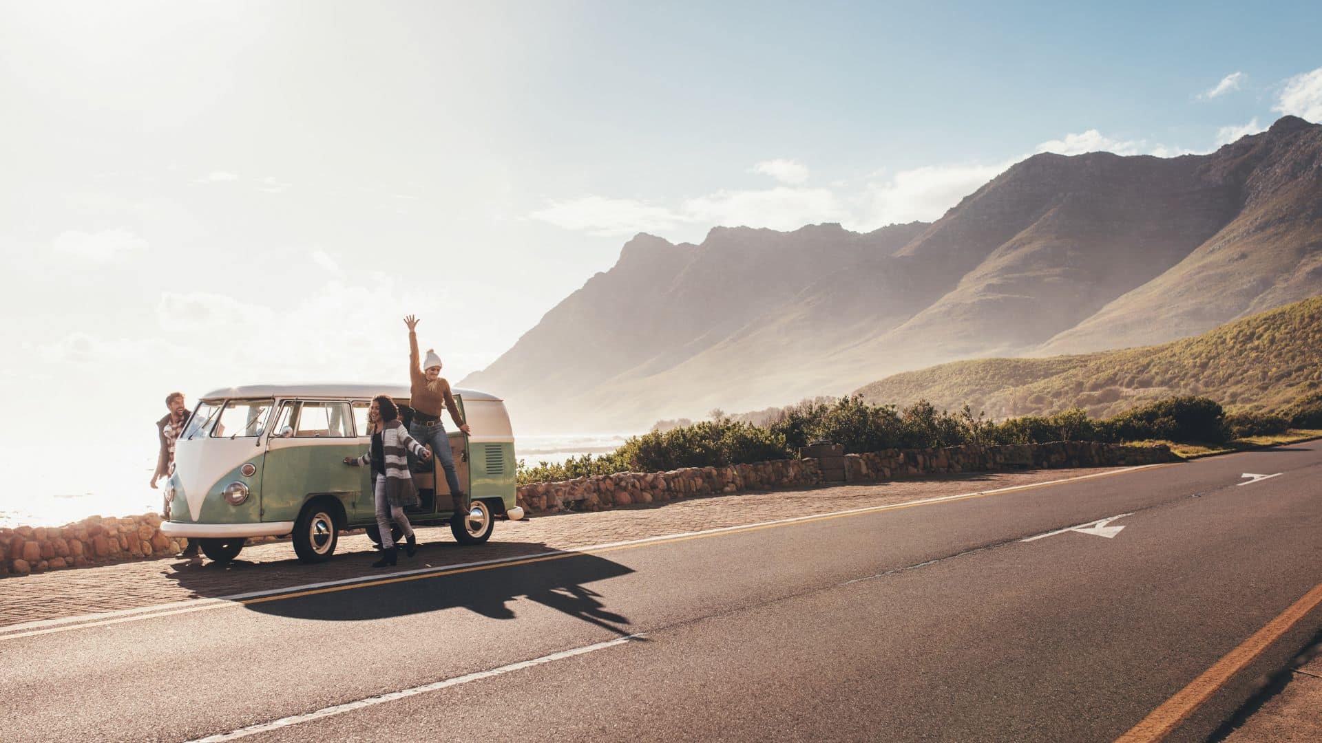 Voyageurs en van vintage sur une route côtière bordée de montagnes en Nouvelle-Zélande lors d’un road trip.