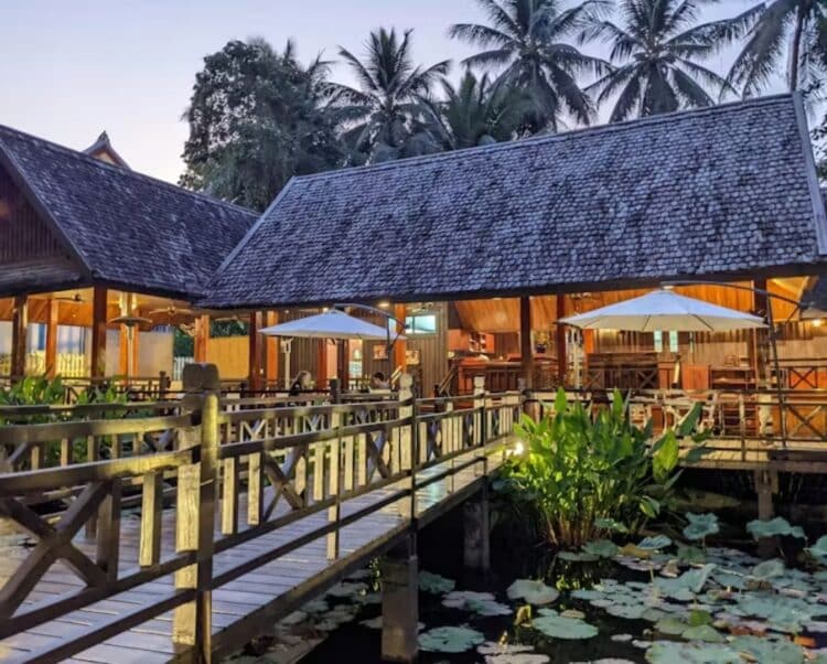 Restaurant du Parasol Blanc Hotel avec terrasse en bois, tables dressées et ambiance tropicale.