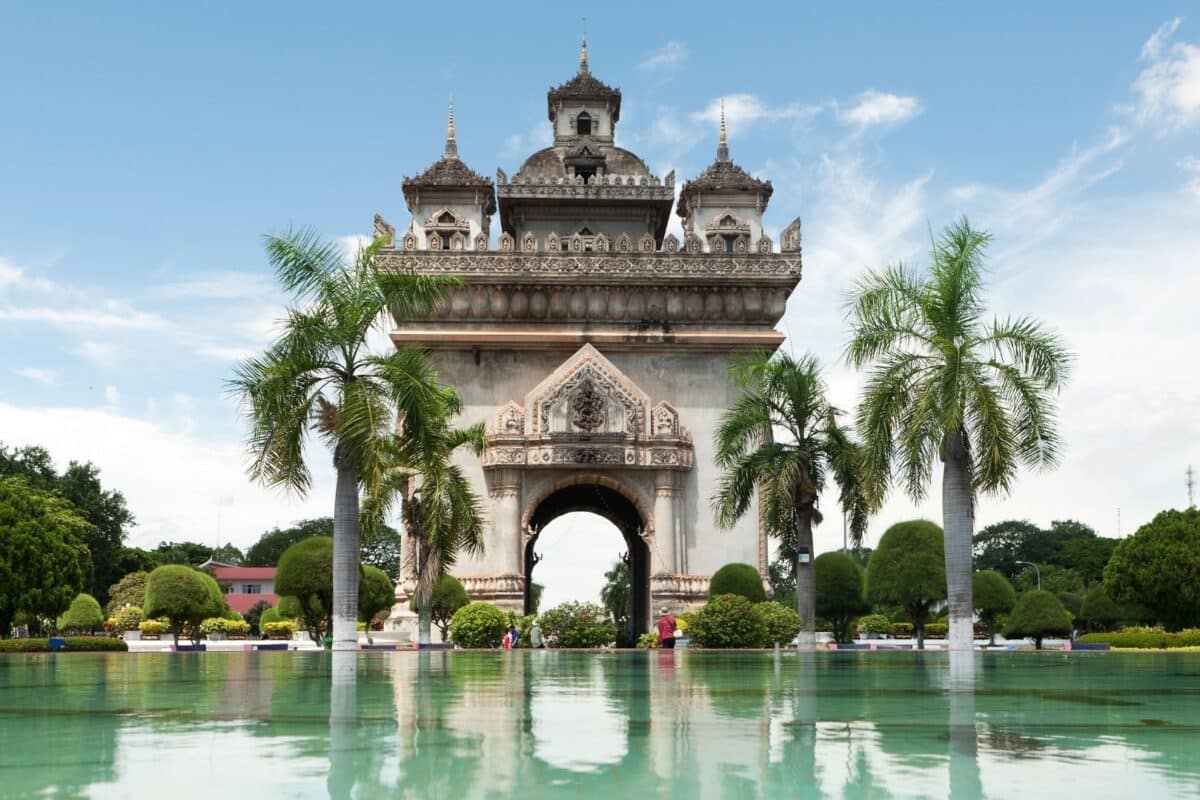Monument du Patuxai à Vientiane entouré de palmiers et reflété dans un bassin.