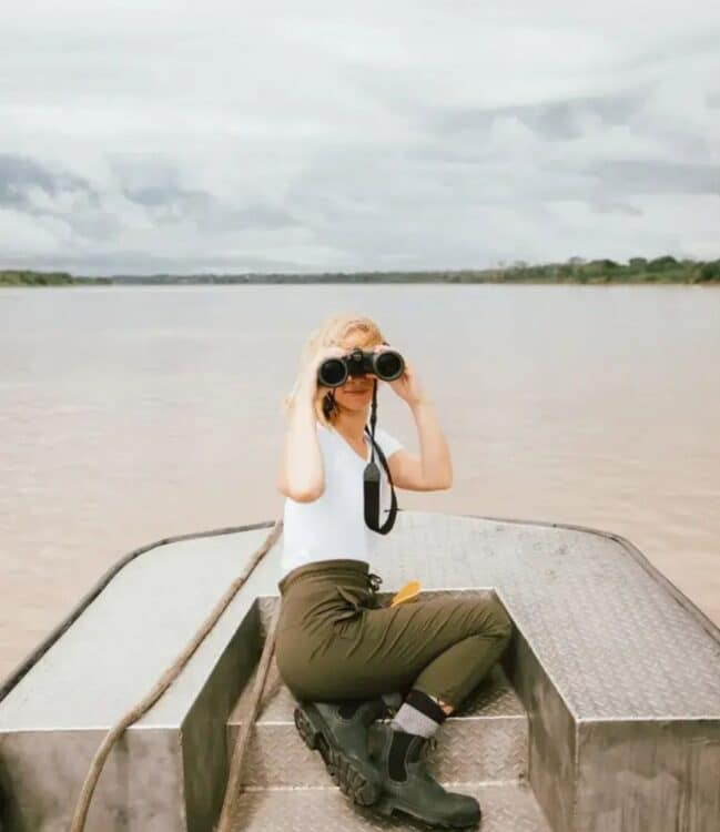 Voyageuse observant la nature avec des jumelles depuis une petite embarcation sur un fleuve d’Amazonie peruvienne.