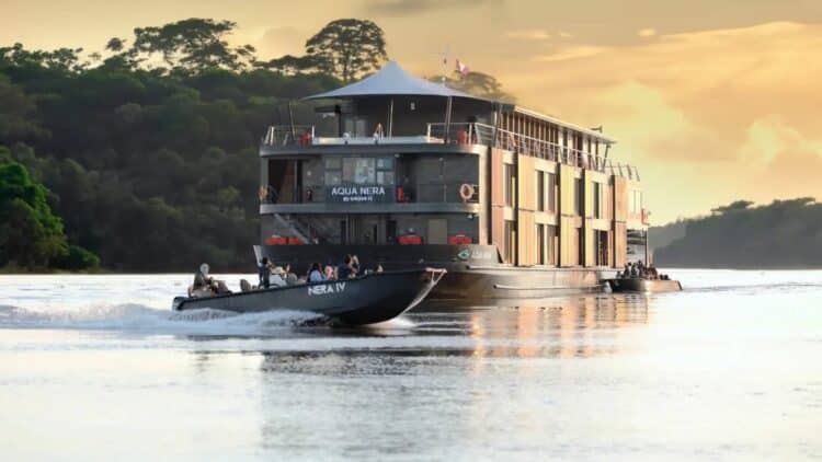 Bateau de croisiere Aqua Nera naviguant au coucher du soleil sur un fleuve d’Amazonie avec petite embarcation au premier plan.