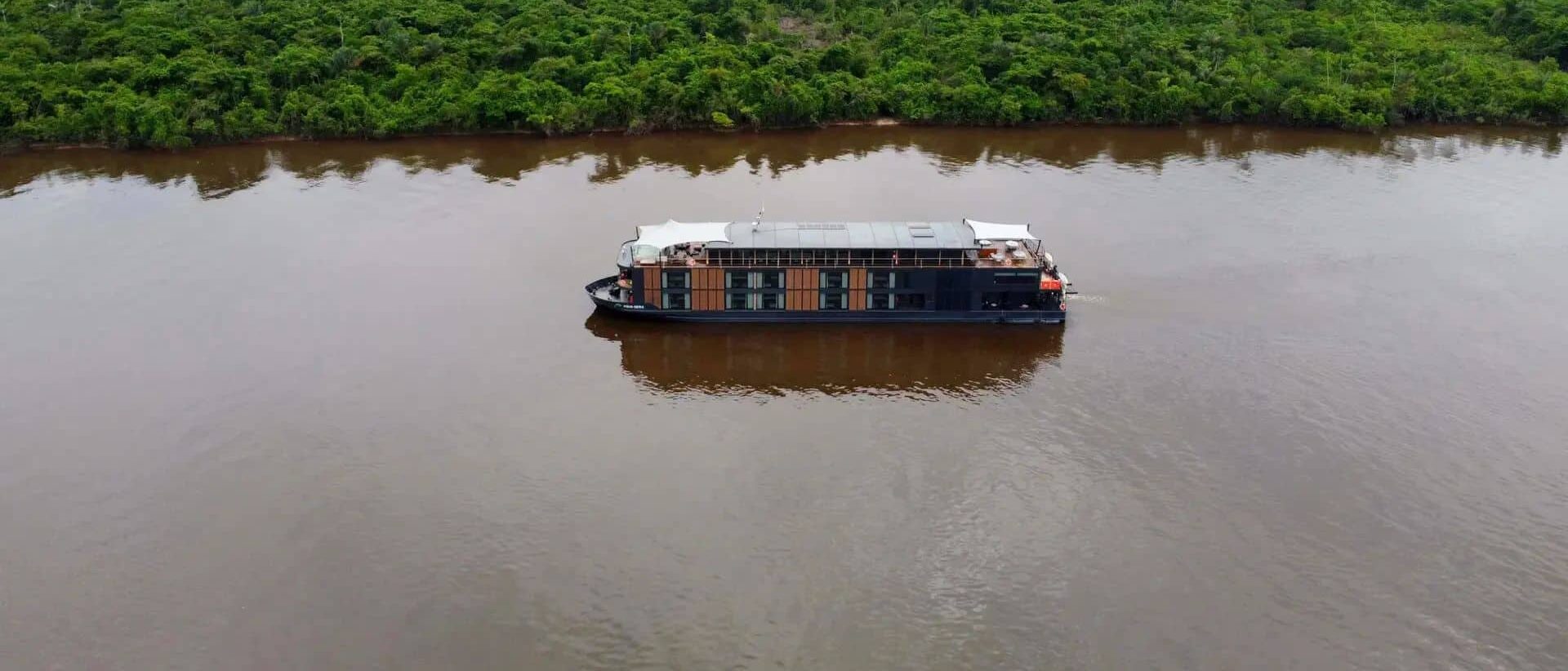 Bateau lodge naviguant sur un large fleuve en pleine Amazonie peruvienne entoure de foret tropicale dense.